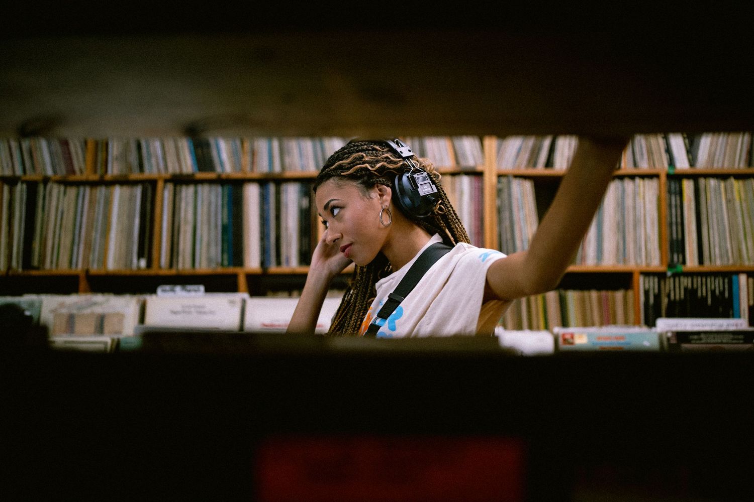 Young woman with braids and headphones searches through vinyl records on shelves in a record shop.