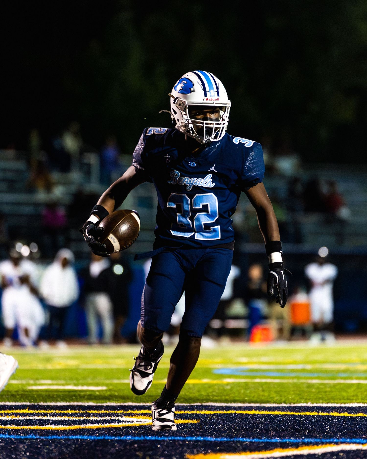 Football player #32 in navy uniform carries ball during night game.