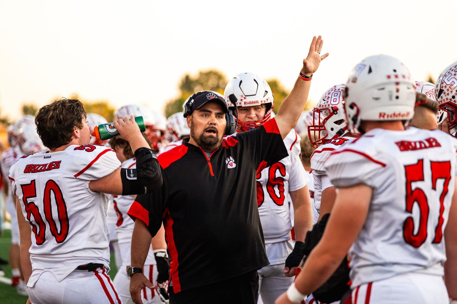 Football coach in red and black celebrates with players on the sideline during a game.