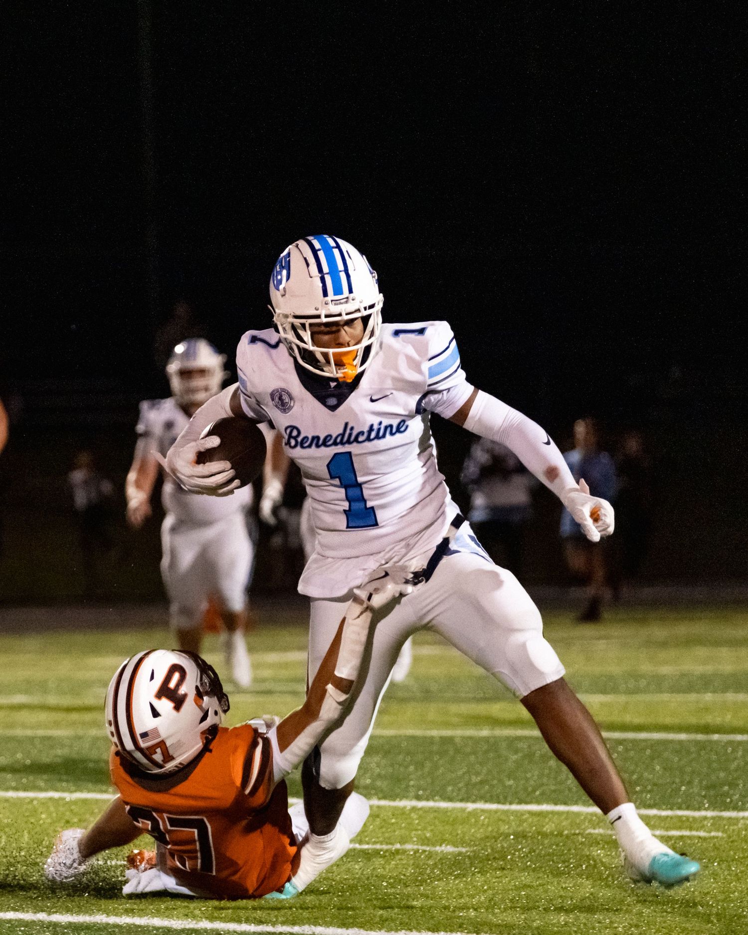 Benedictine football player number 1 breaks a tackle during an intense game.