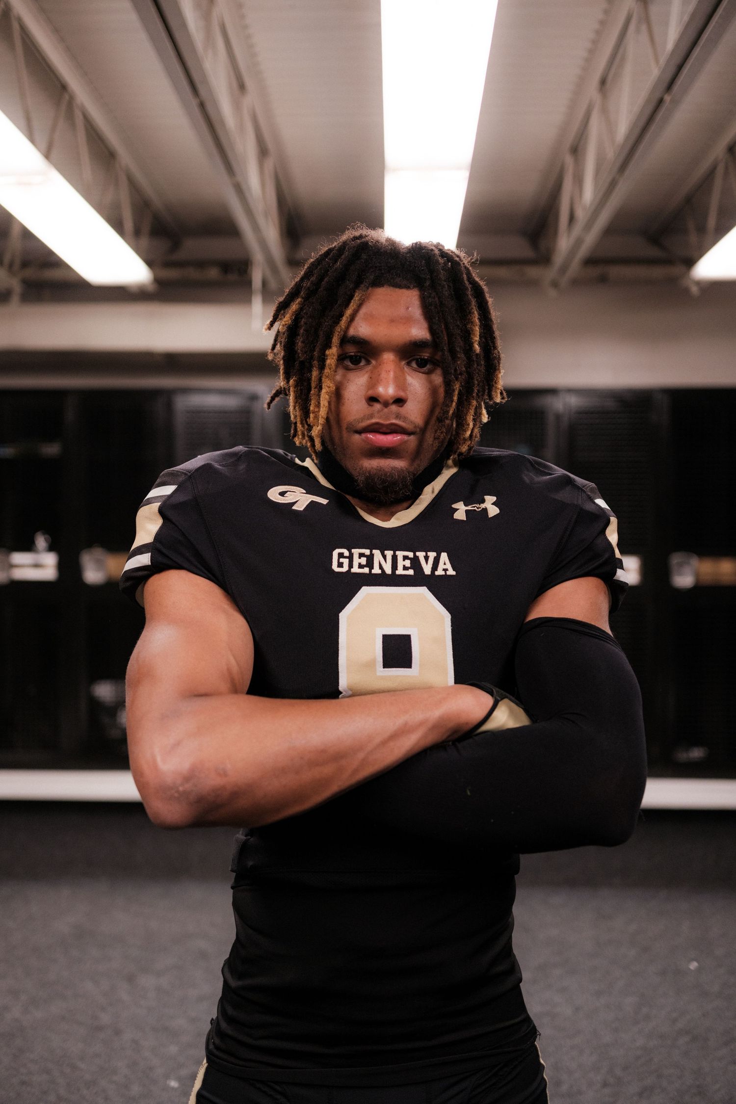 Geneva College football player number 8 stands with arms crossed in the locker room.