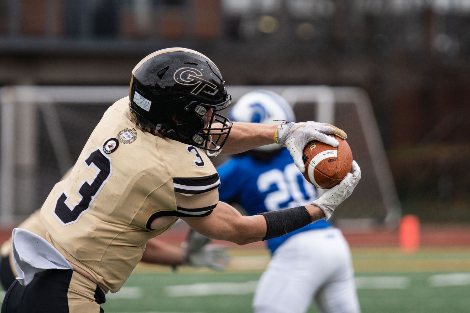 Geneva College football player number 3 in gold uniform catches ball during game.