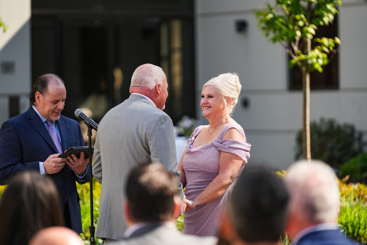 Outdoor wedding ceremony with an officiant reading vows as the couple stands together before guests.