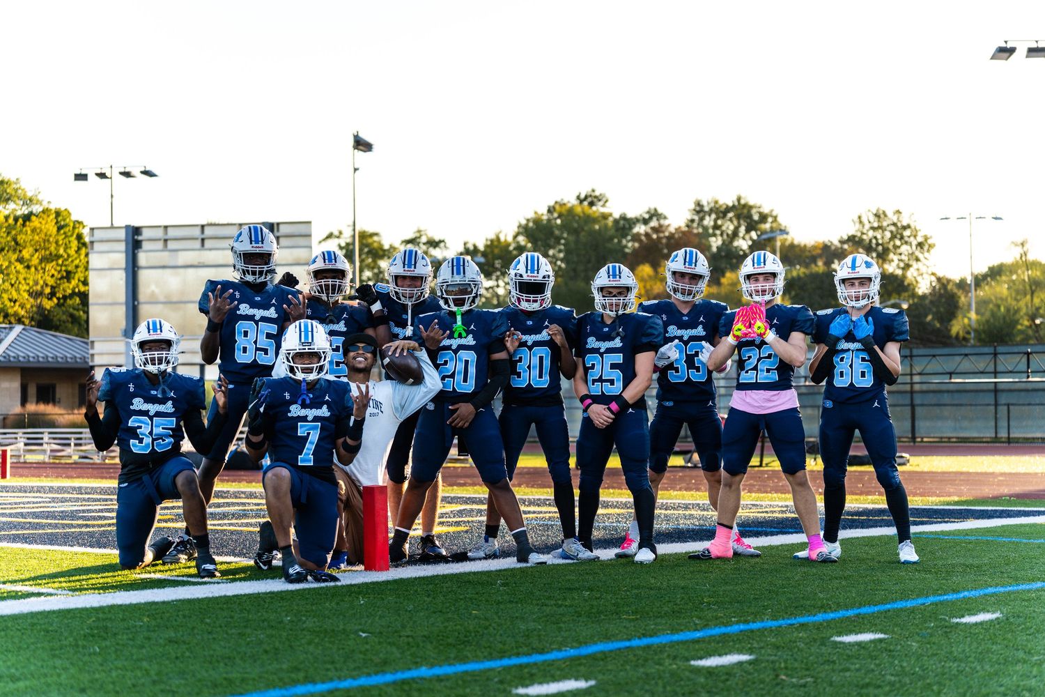 High school Bengals football team poses together on turf field during sunny afternoon game day.