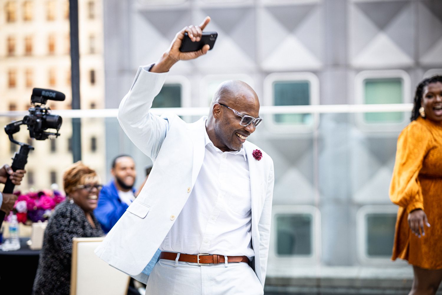 Man in white suit dancing joyfully at outdoor celebration event in urban setting.