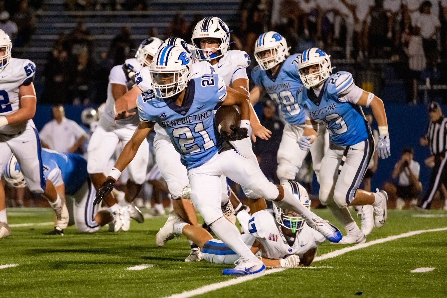 Benedictine player number 21 in light blue runs with ball during night football game.