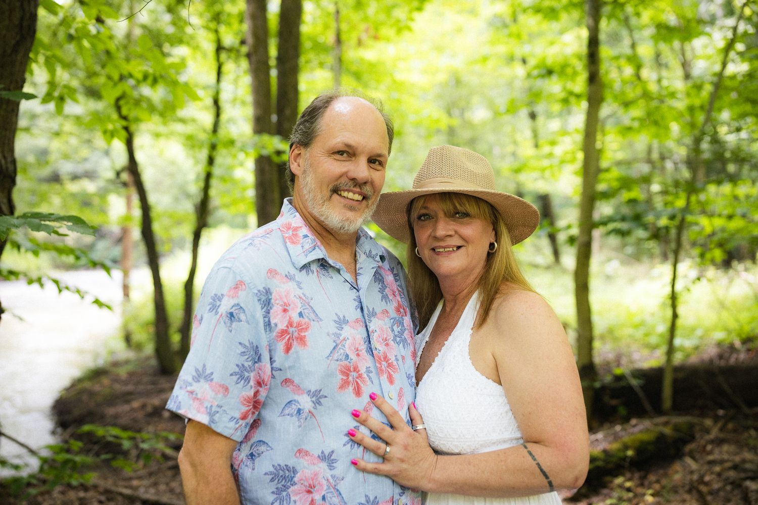 Smiling mature couple posing together in a lush green forest, woman wearing a straw sun hat.