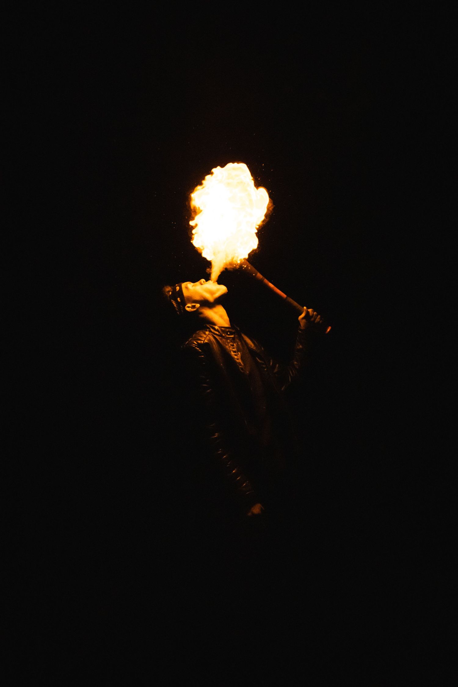 Fire breather performing dramatic flame stunt against dark black night background.