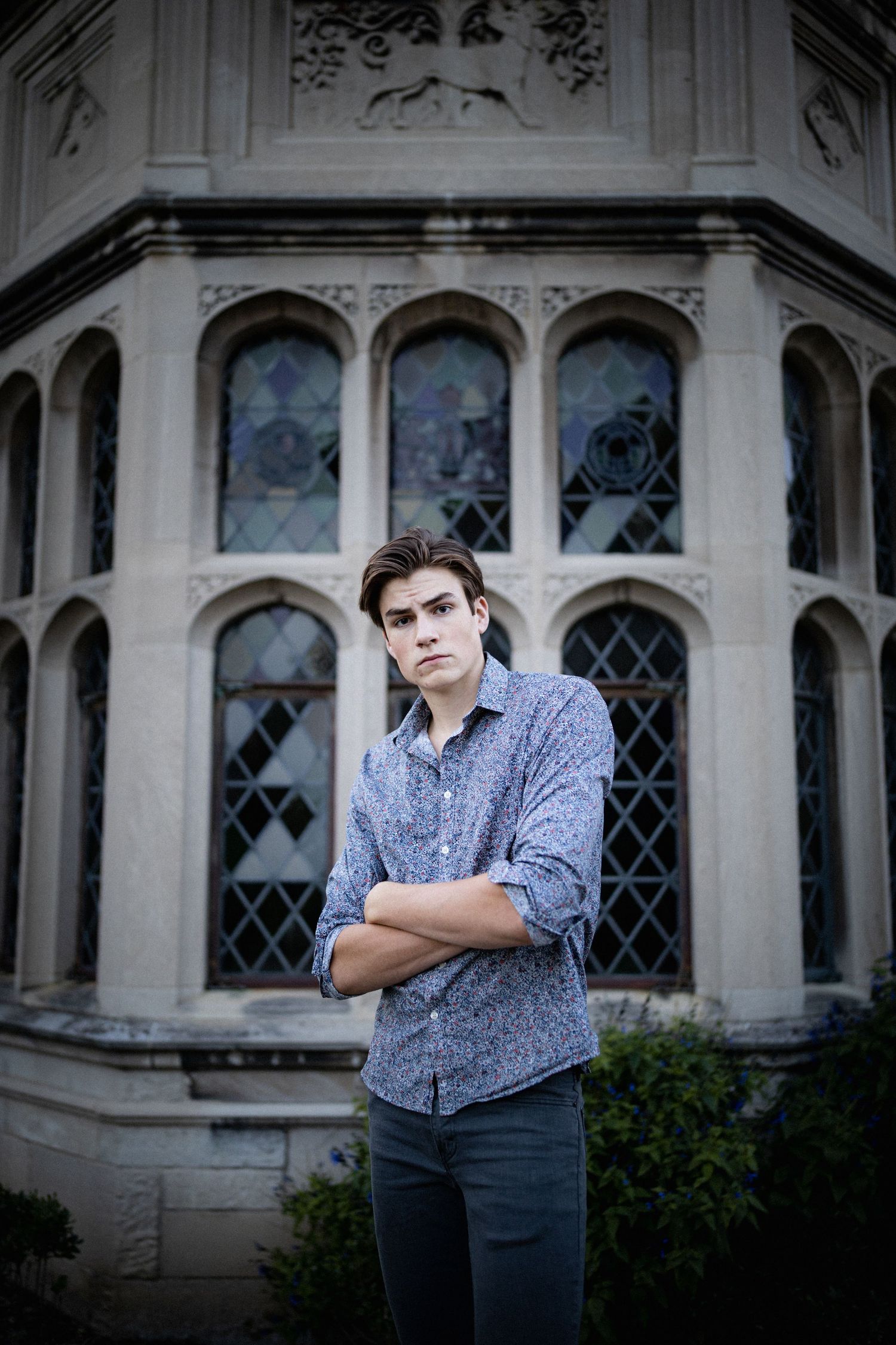 Young man with arms crossed stands confidently before ornate Gothic architecture building.