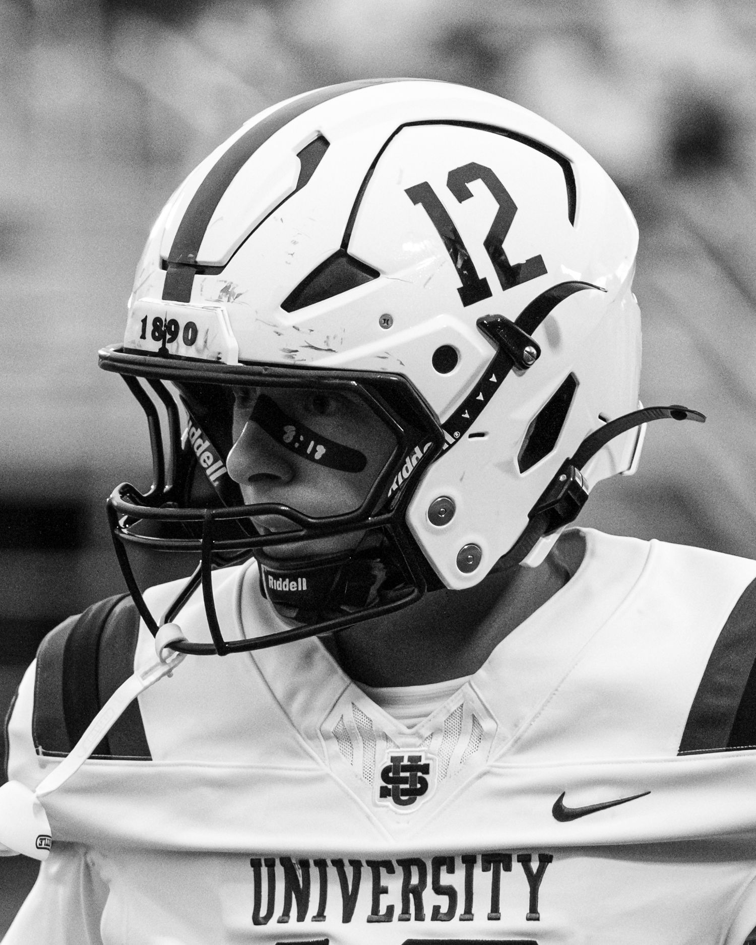 Black and white close-up of football player wearing number 12 University helmet.