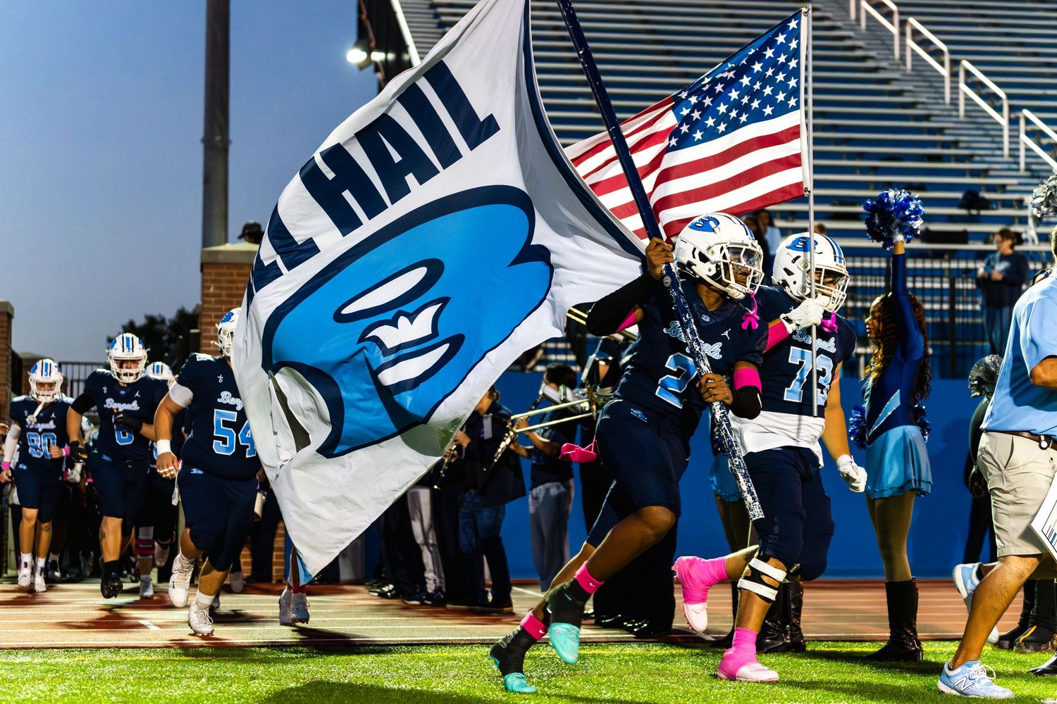 Bengals football players run onto field carrying team flag and American flag before home game.