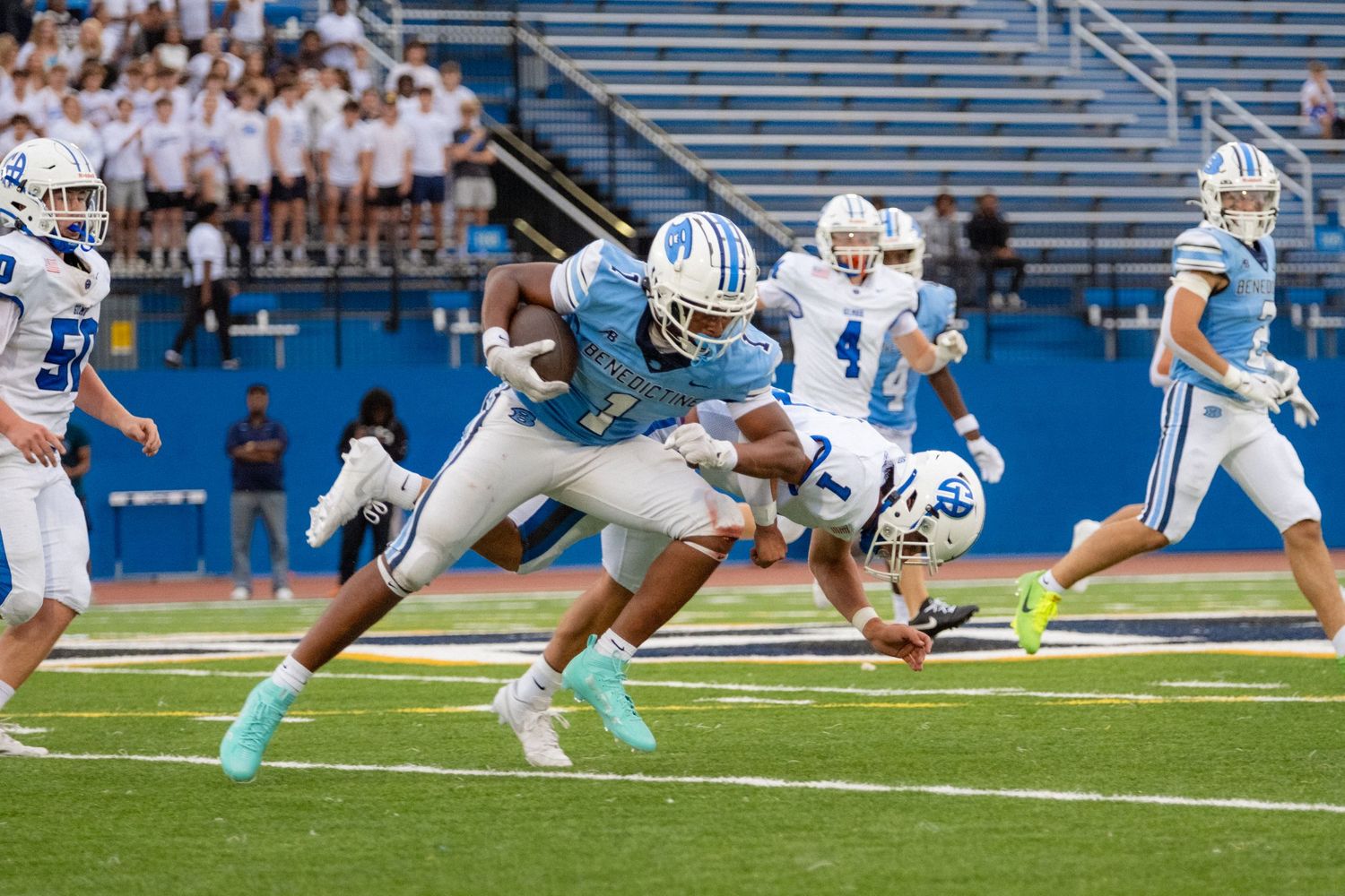 Benedictine football player breaks through a tackle during a daytime game on blue field.