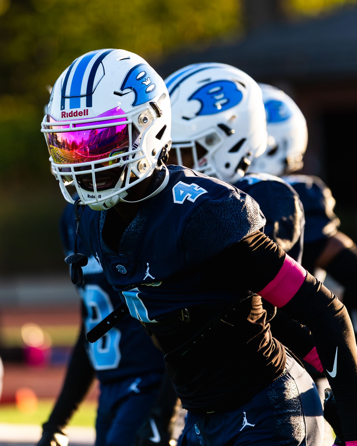 Football player in dark blue Riddell helmet with iridescent visor in game action.