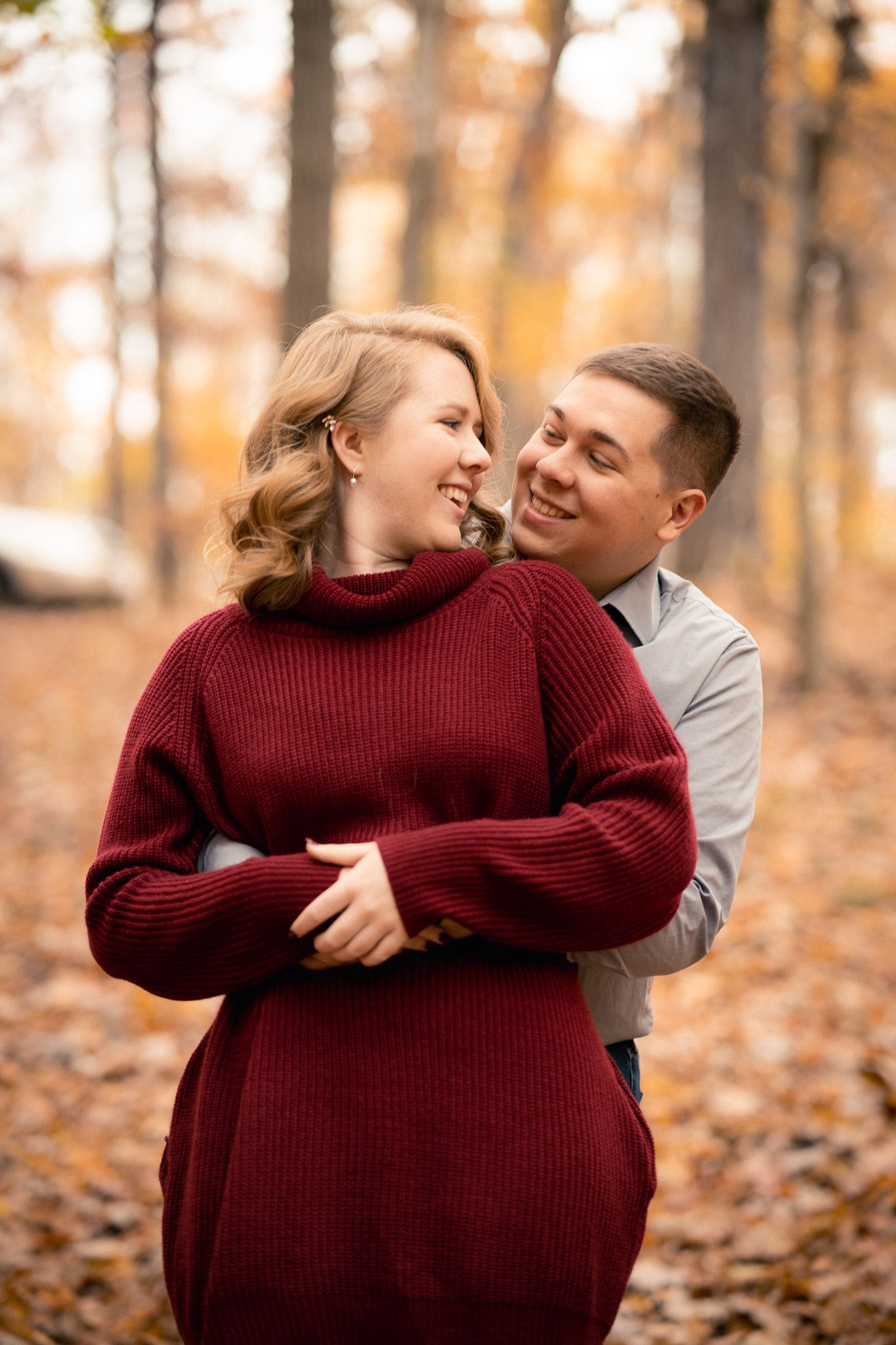 Couple embracing and smiling together in a colorful autumn forest setting.