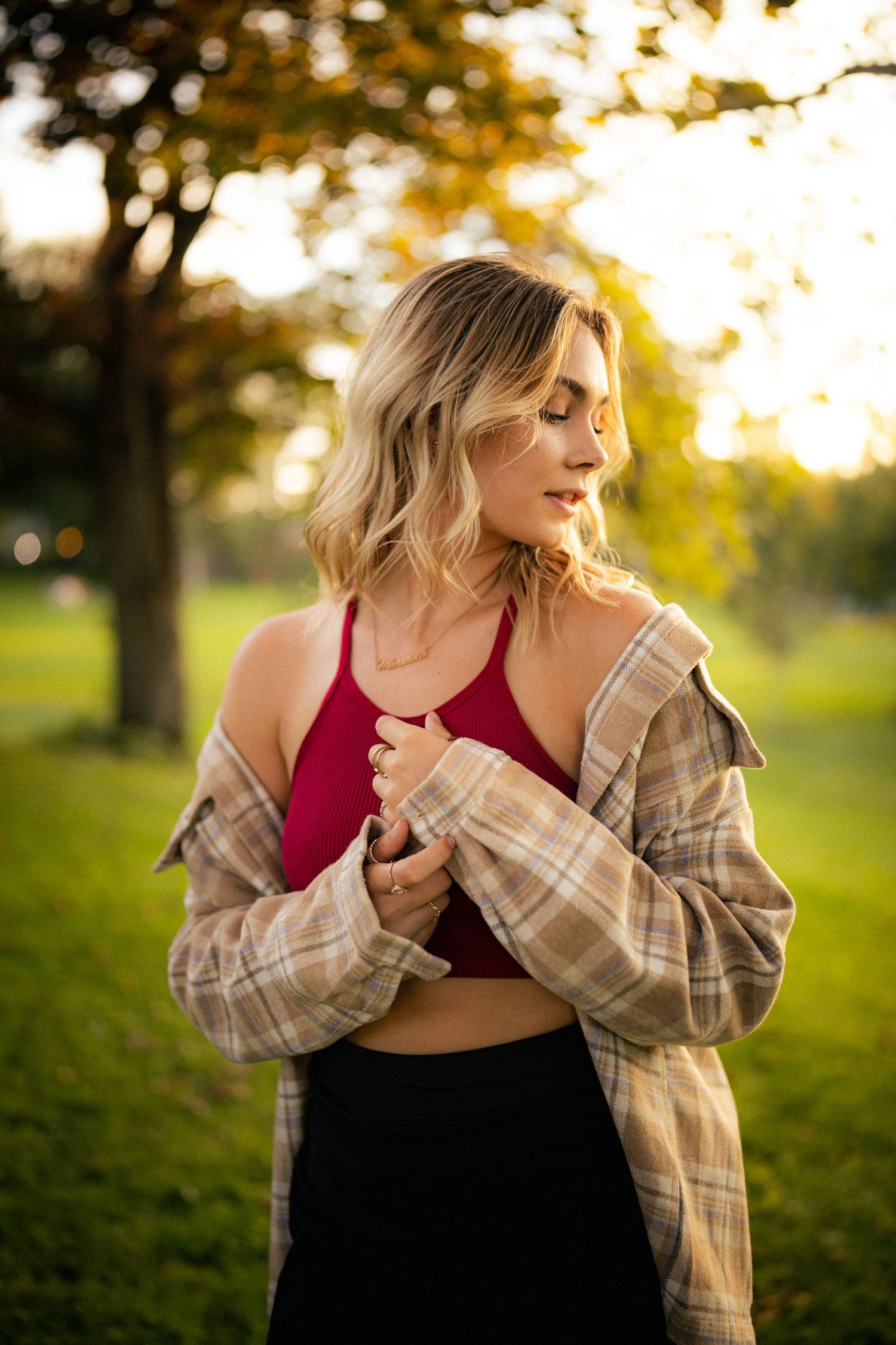 Young blonde woman in red crop top and plaid shirt posing in golden sunset light in park.