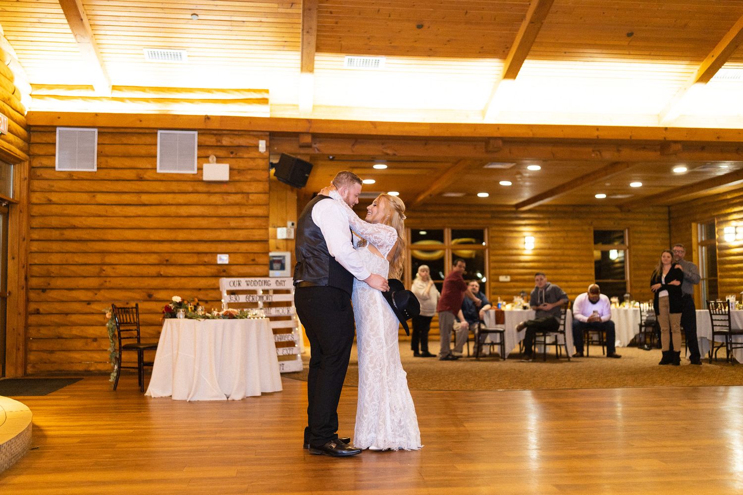 Bride and groom sharing their first dance in a warmly lit rustic log cabin wedding reception venue.