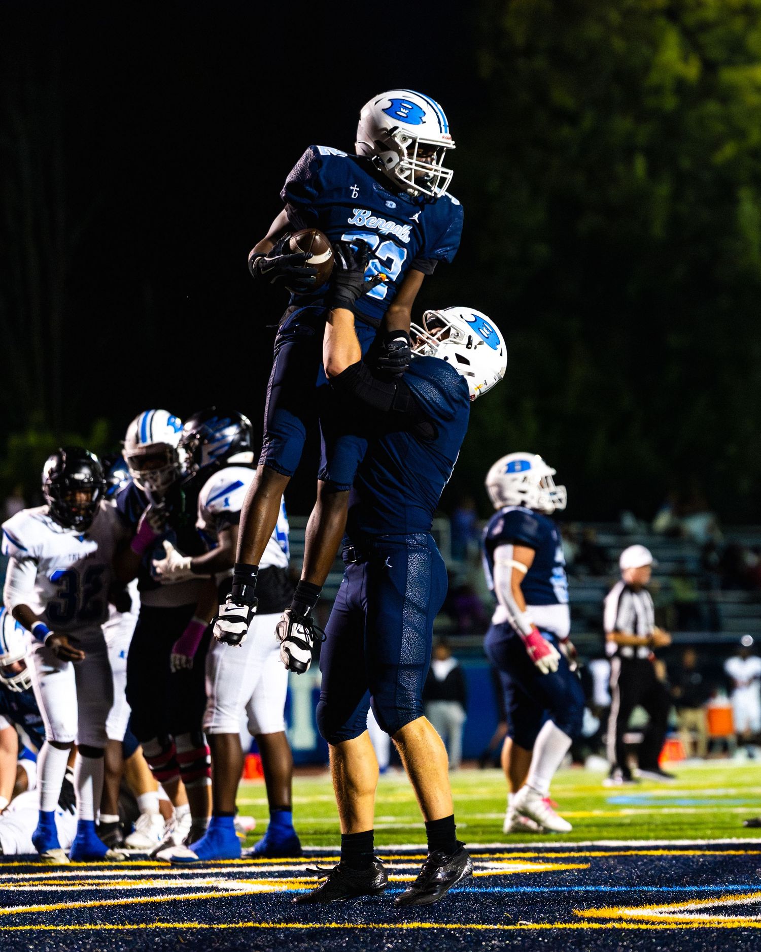 Football players celebrate touchdown with lift during night game.