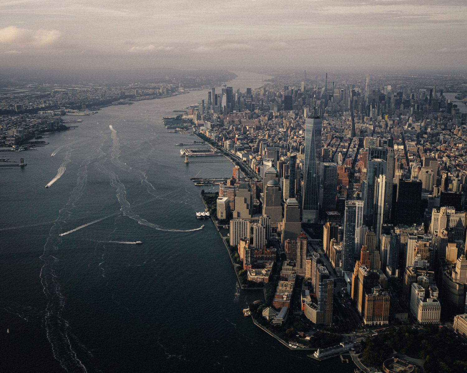 Aerial view of Lower Manhattan skyline surrounded by Hudson River and New York Harbor at dusk.