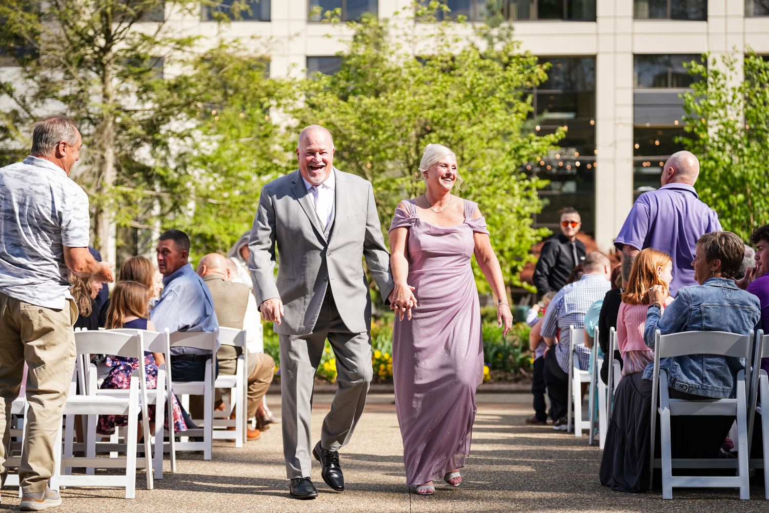 Elegant couple walking down the aisle at an outdoor wedding ceremony surrounded by seated guests.