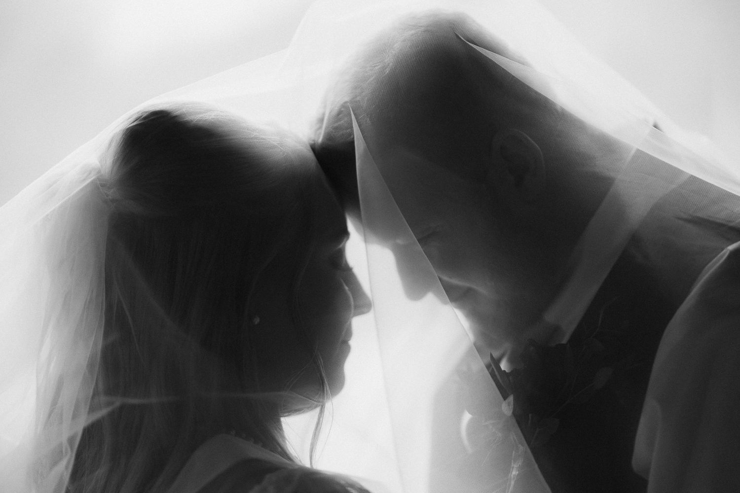 Romantic black and white photo of bride and groom sharing an intimate moment under a flowing veil.