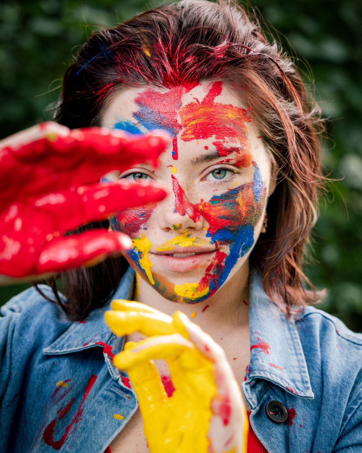 Creative woman covered in colorful red, blue and yellow paint holds painted hands up.