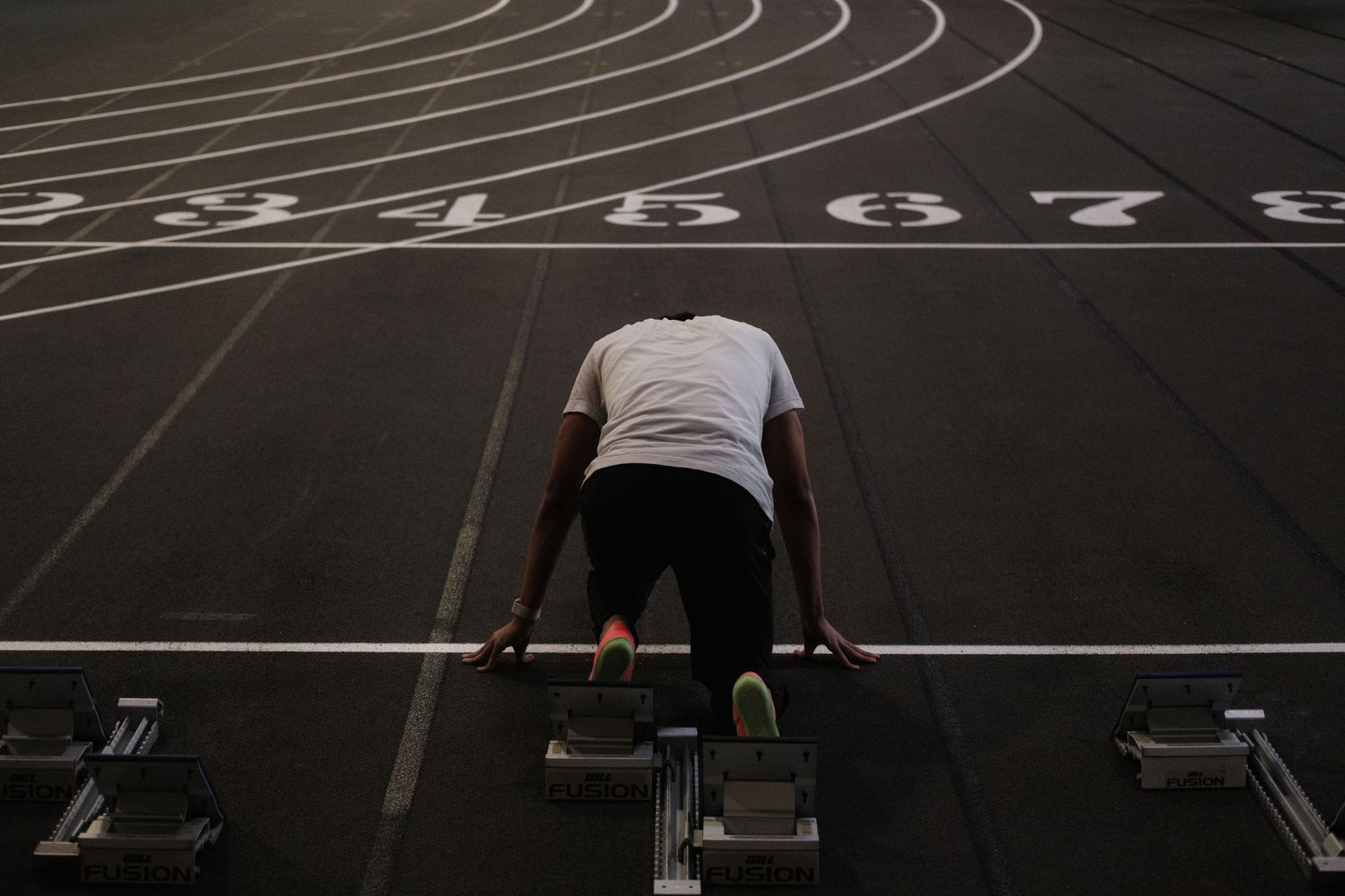 Male athlete in starting position on numbered track lanes at an outdoor running track.