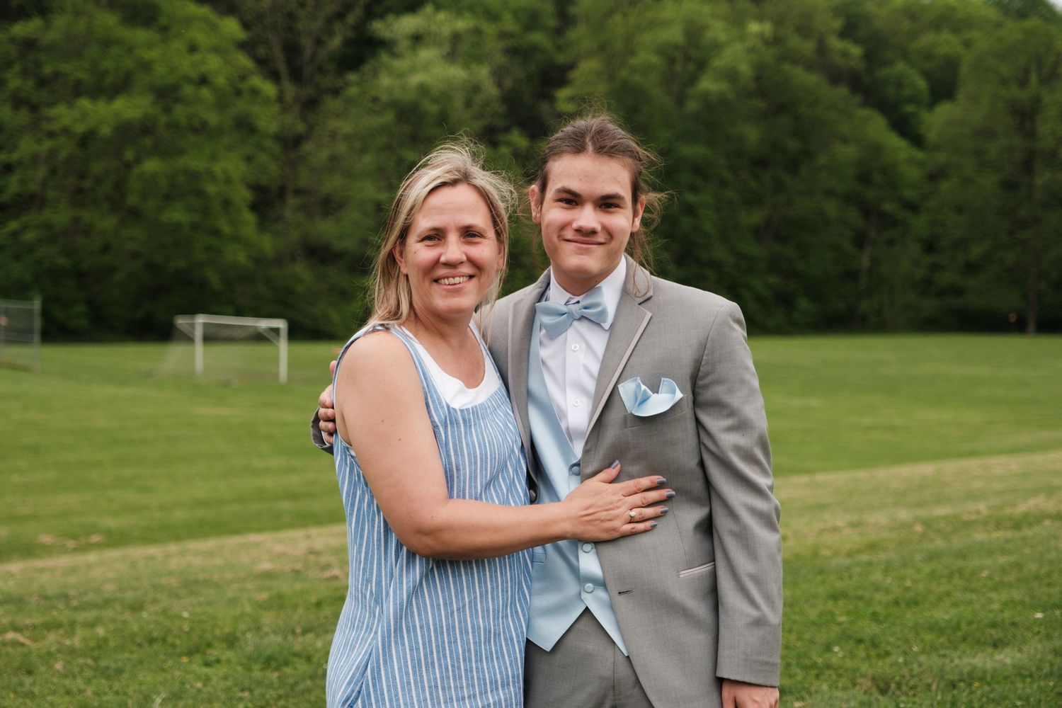 Mother and son pose together on green field, son dressed in gray prom suit.