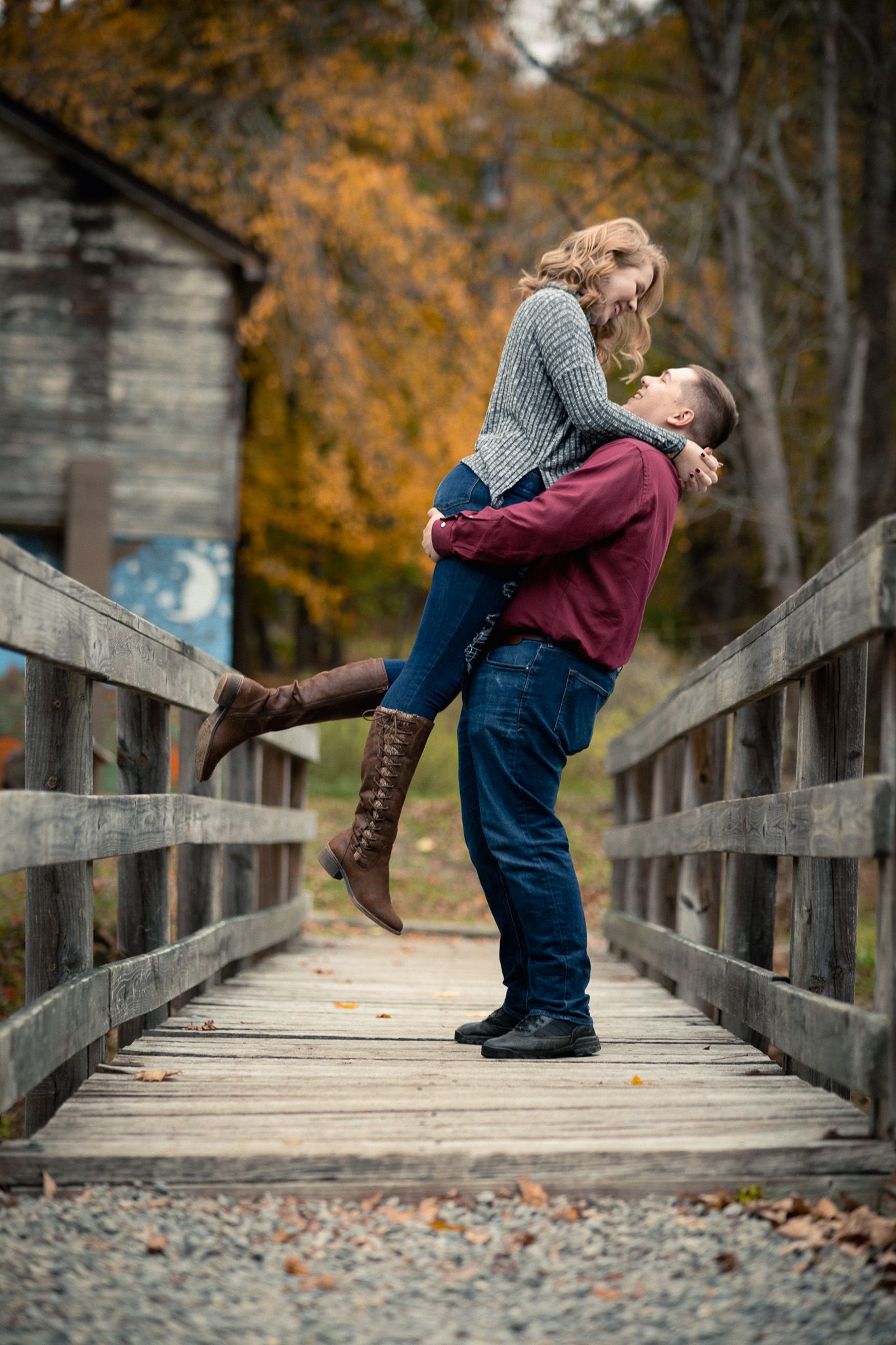 Man lifting and spinning his partner on a wooden bridge during a fall engagement photo session.