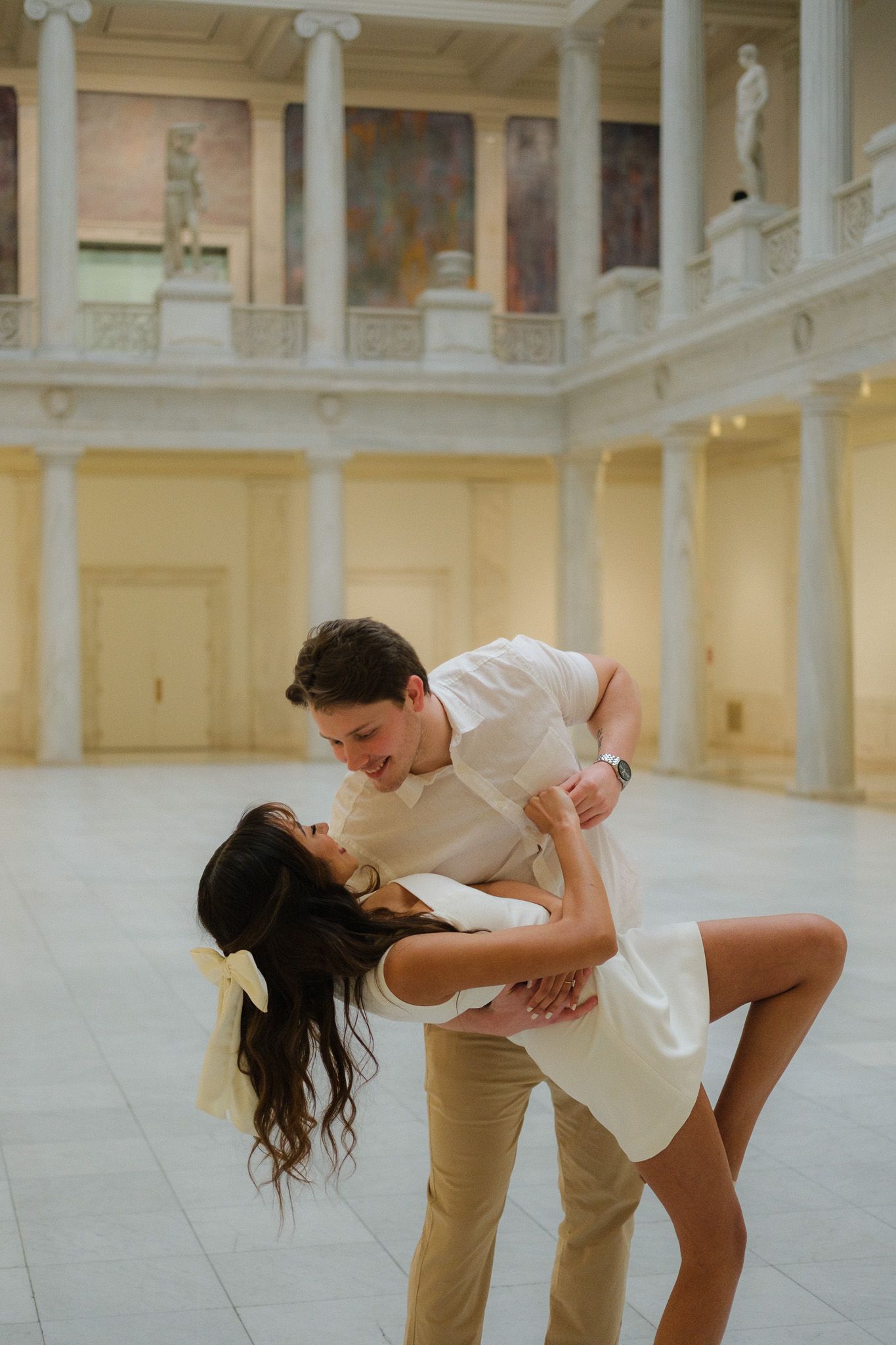 Couple performing romantic dip dance move inside elegant classical museum atrium with columns.