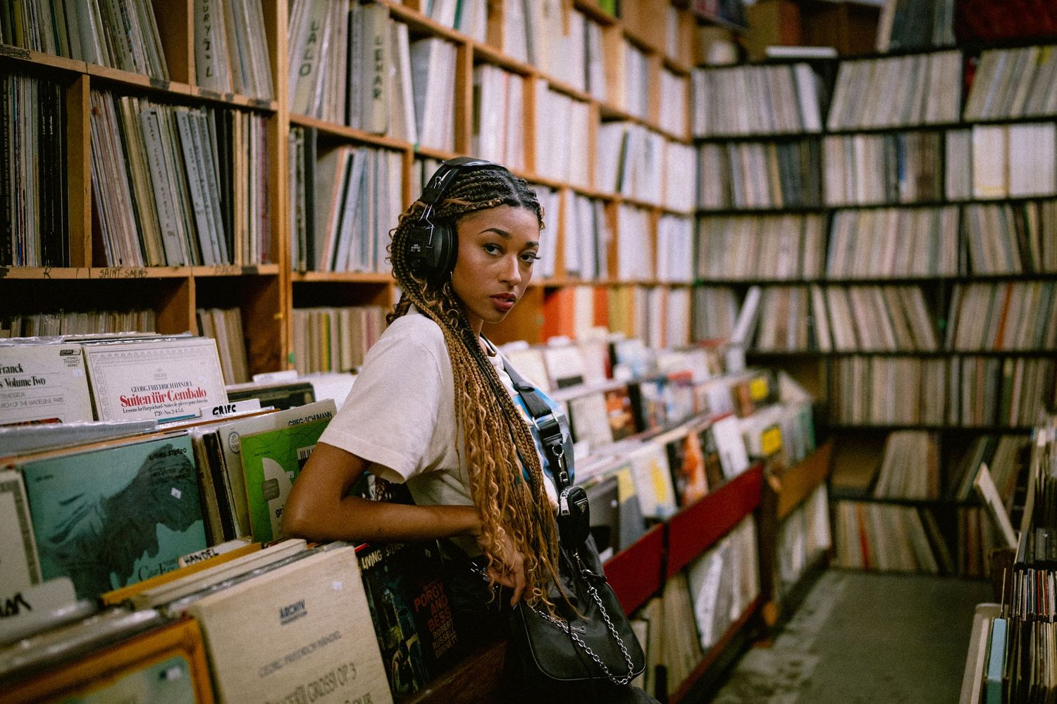 Young woman with braids and headphones browses vinyl records in a music record store.