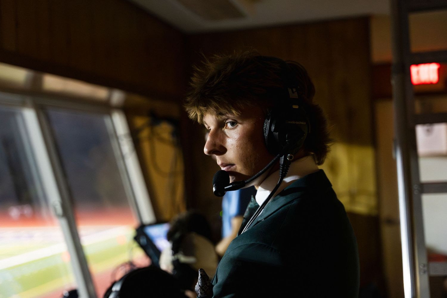 Young male broadcaster wearing headset works in press box.