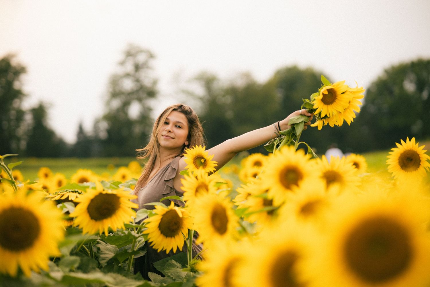 Young blonde woman reaching out to touch sunflowers while standing in a vibrant yellow sunflower field.