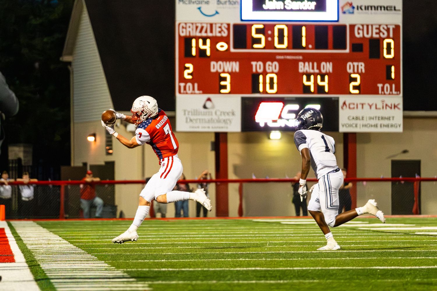 Football player in red uniform catches pass near end zone with scoreboard showing Grizzlies leading 14-0.