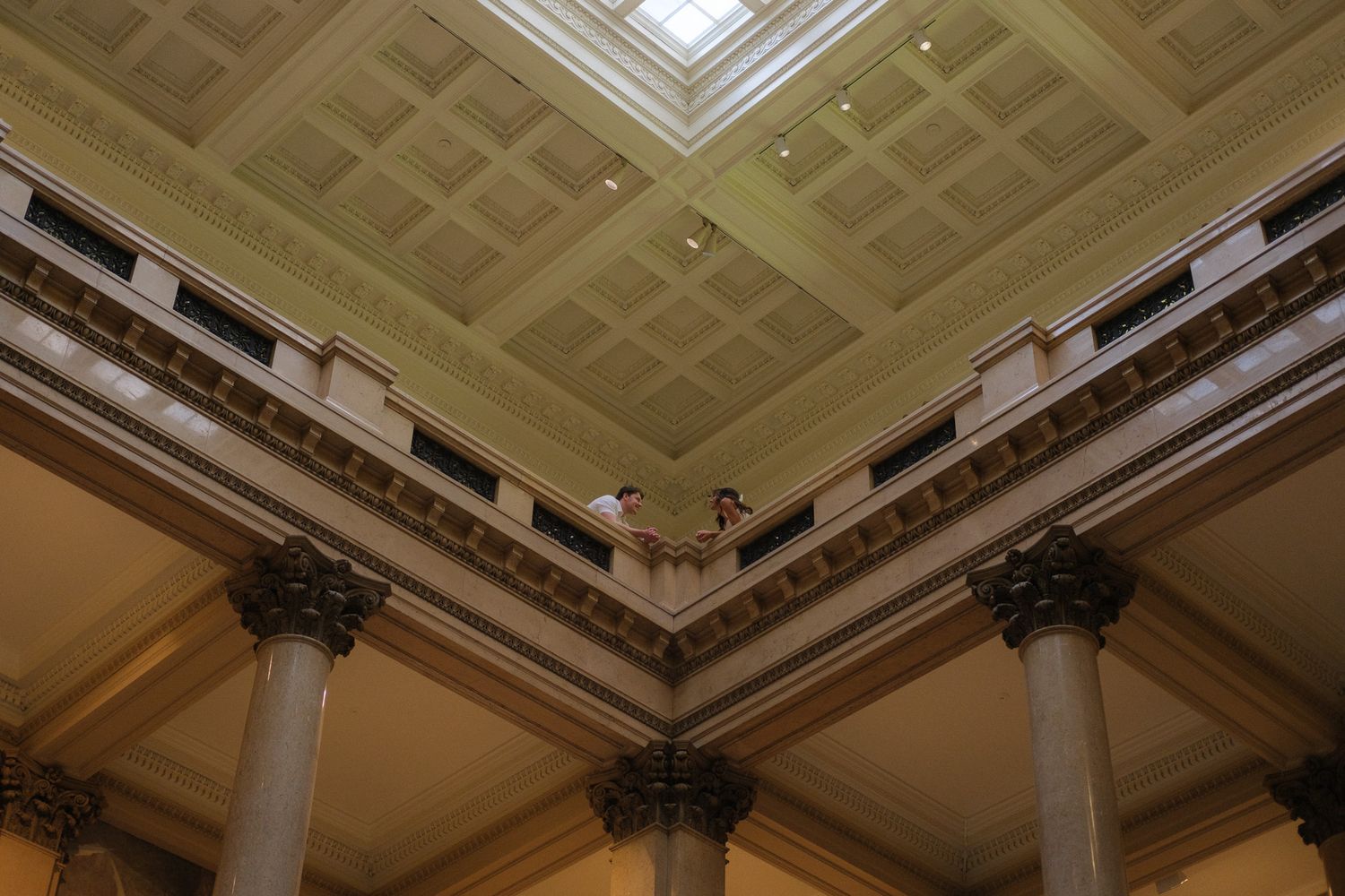 Ornate coffered ceiling with skylight and Corinthian columns in a grand neoclassical building interior.