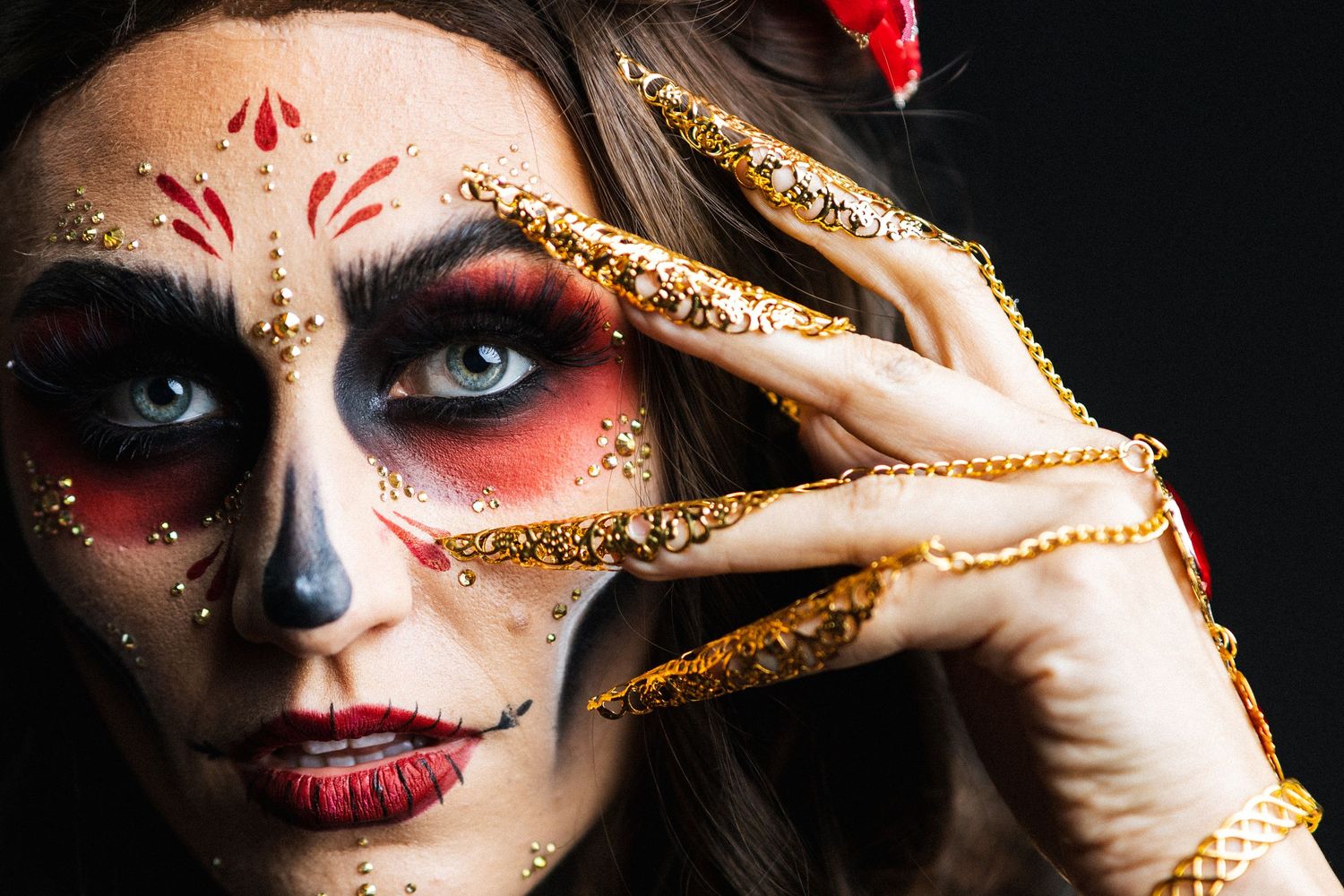 Woman with Day of the Dead sugar skull makeup and gold jeweled long nails poses dramatically.