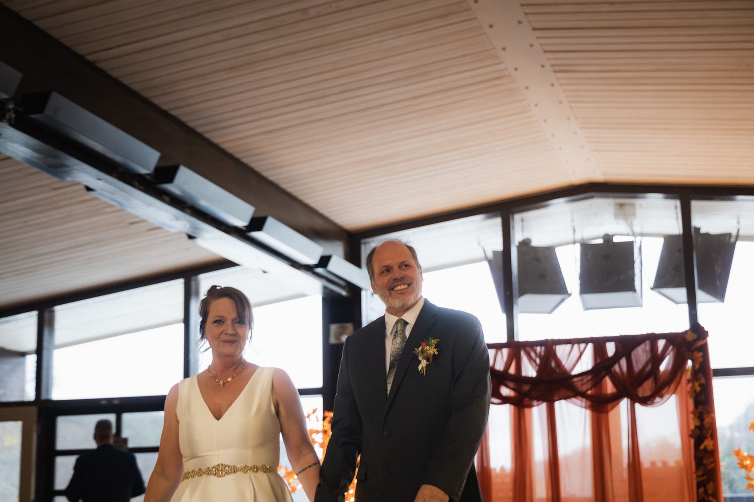 Bride and groom smiling and holding hands at their wedding ceremony in an elegant venue.