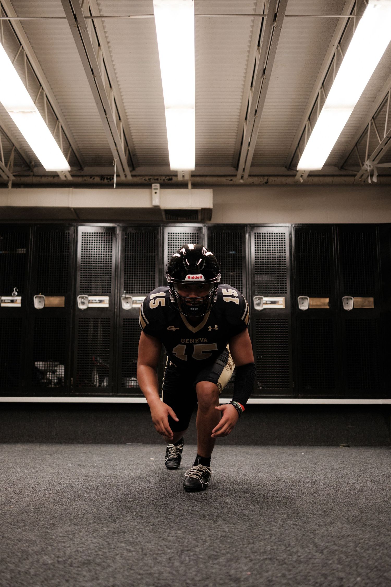 Football player in black Geneva uniform crouches in a dramatic locker room pose.