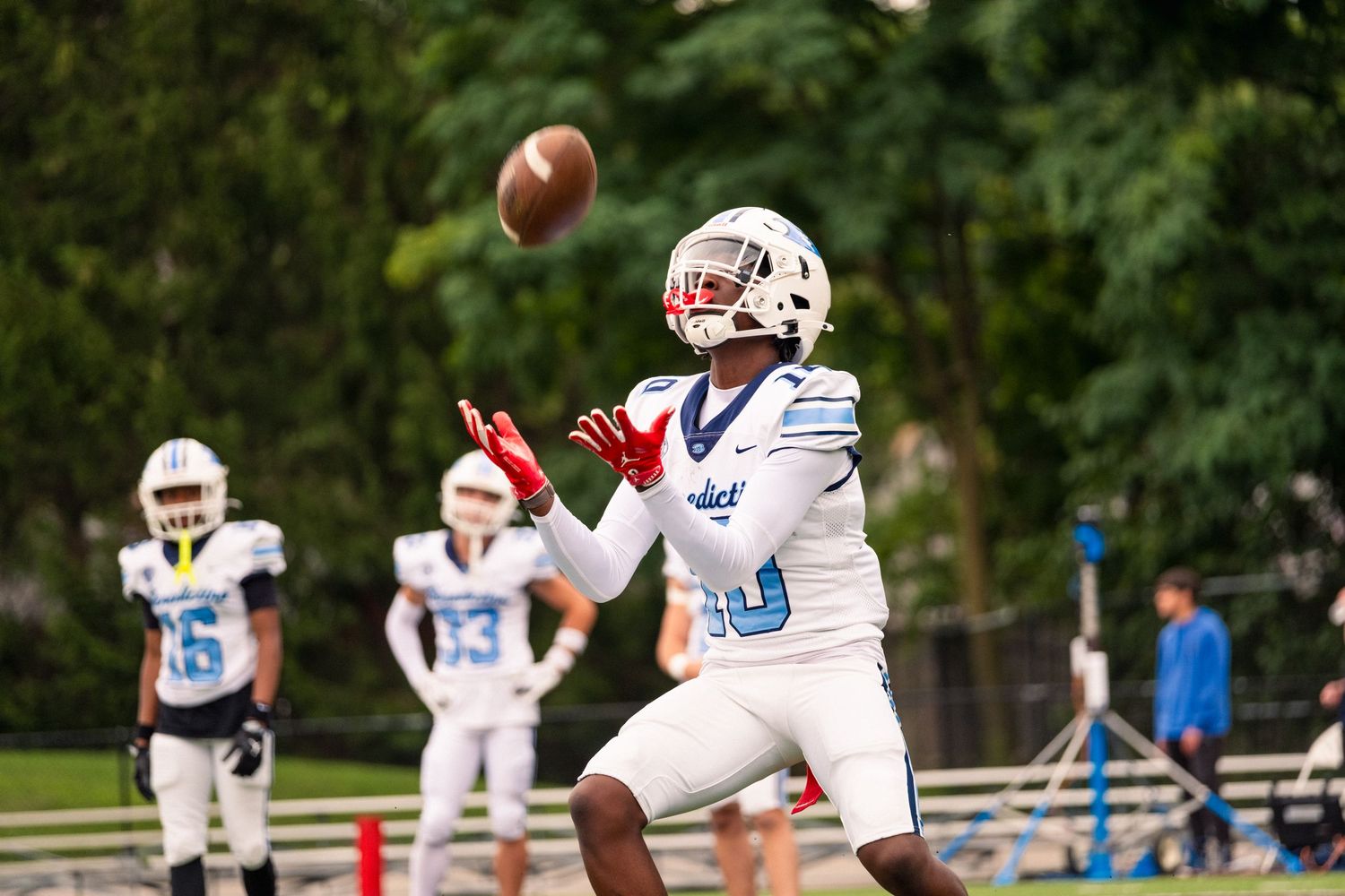Football player in light blue uniform catches a pass during an outdoor game.