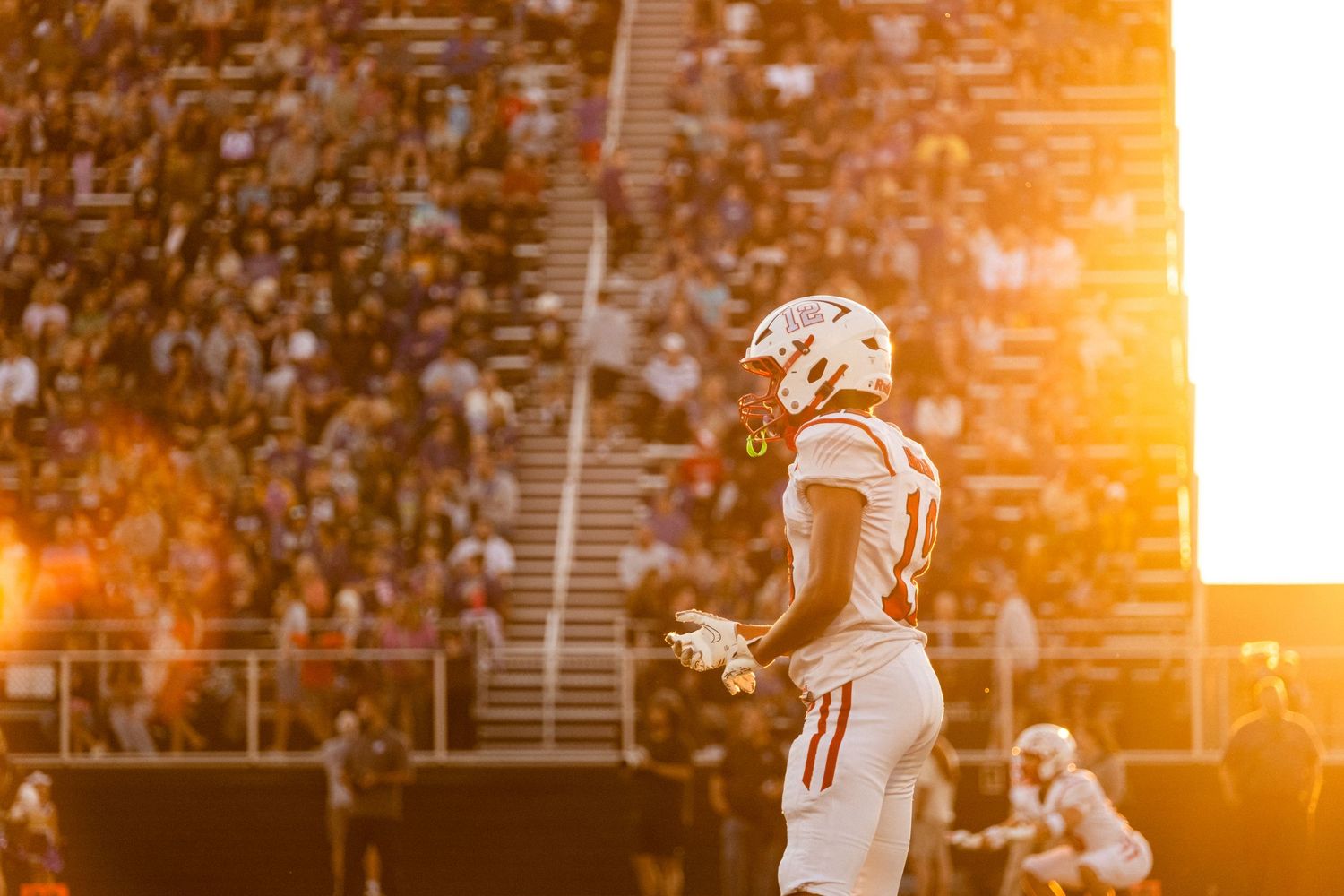 Football player silhouetted against golden sunset light in packed stadium.