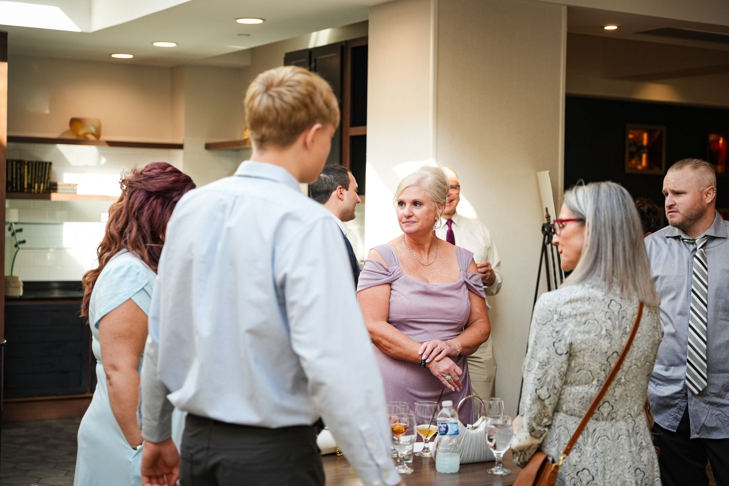Wedding guests mingling and conversing indoors during a reception cocktail hour in a modern venue.