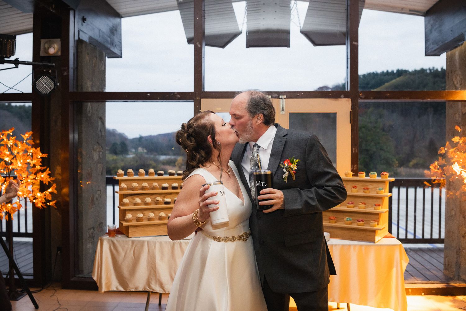 Newlywed couple sharing a romantic kiss at their wedding reception with scenic window backdrop.