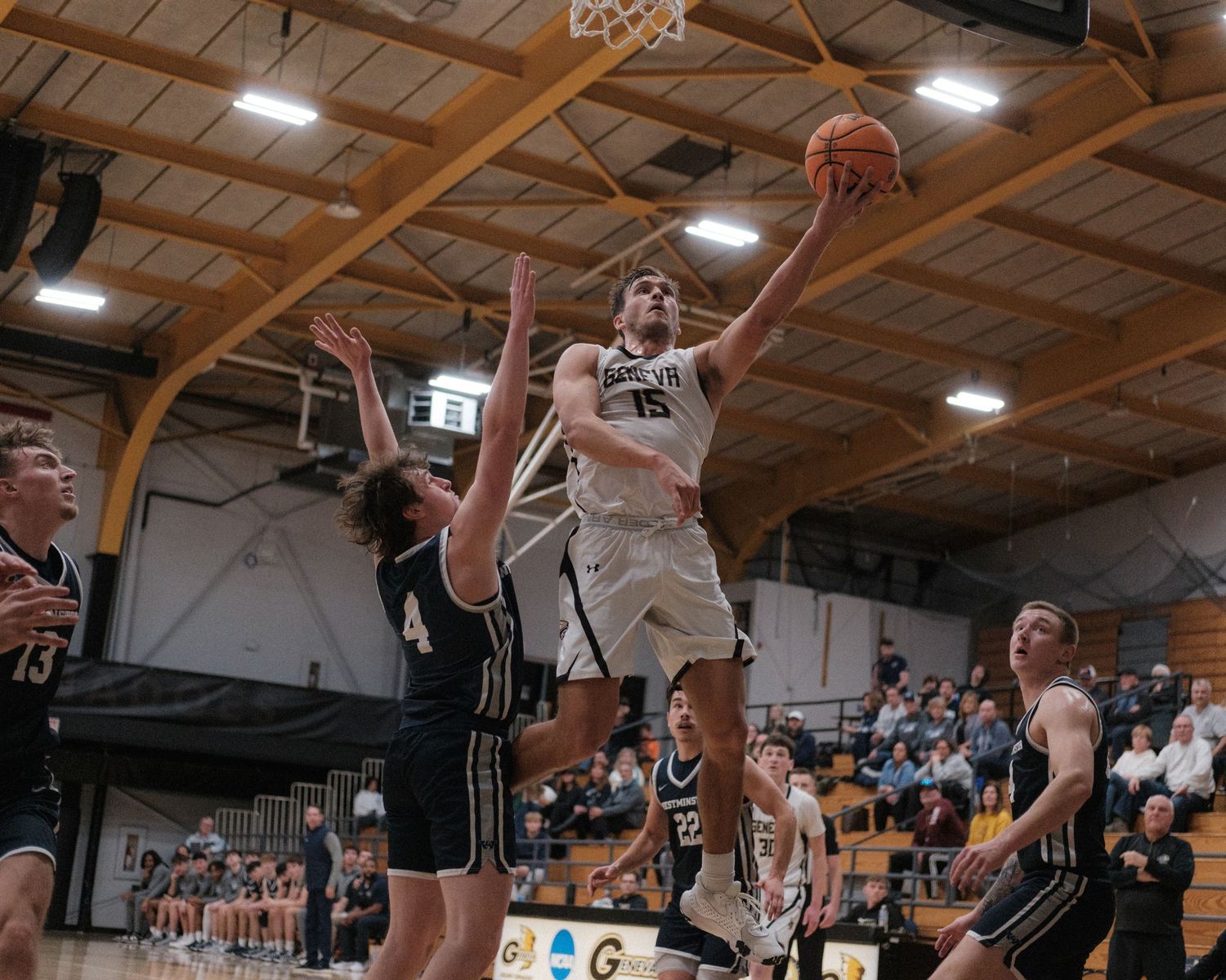 Basketball player number 15 leaping for a layup during an indoor college basketball game.