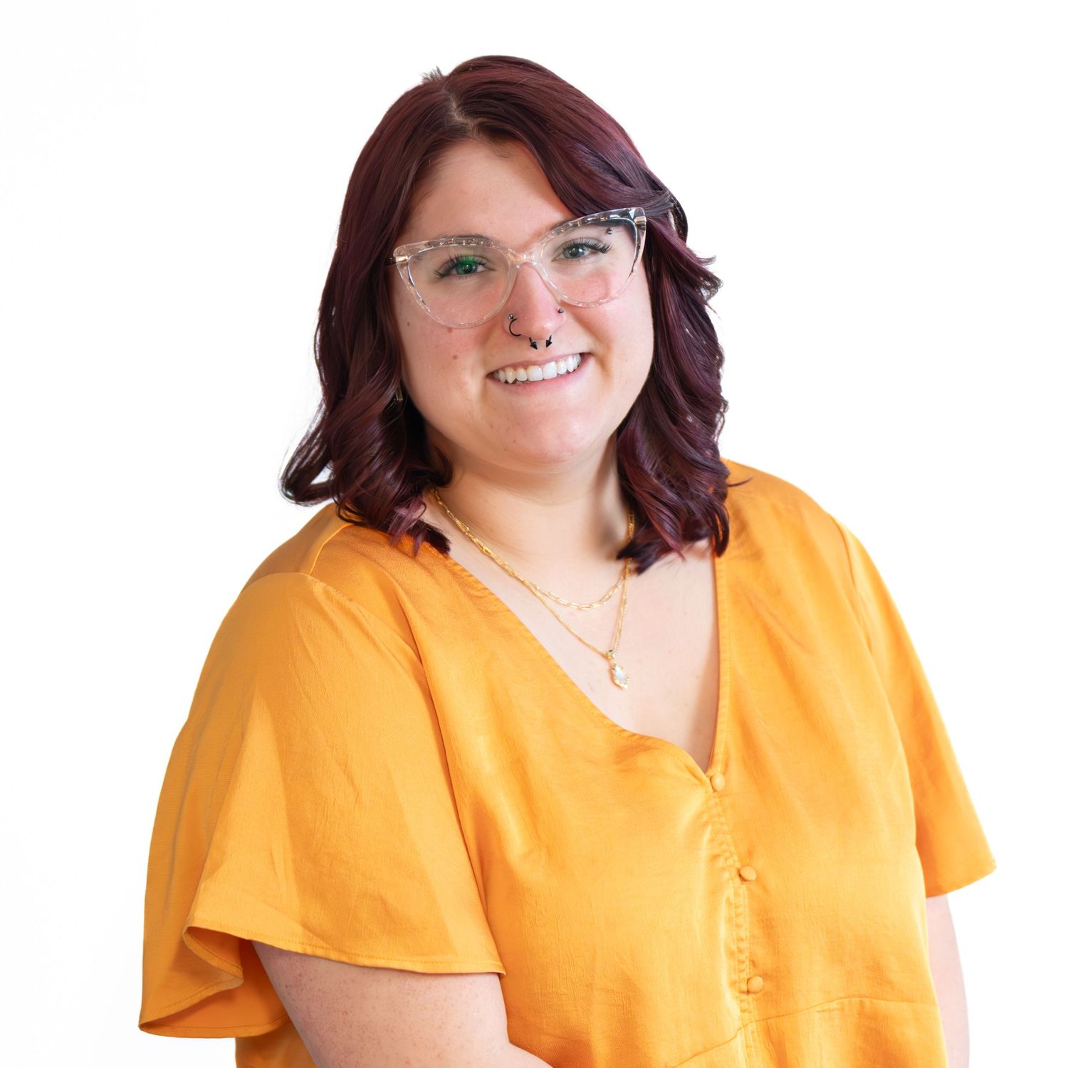 Professional headshot of person wearing yellow top and glasses against white background.