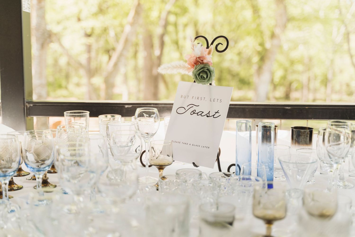 Elegant wedding reception table with crystal glassware, a Toast sign in a decorative holder, and floral centerpiece.