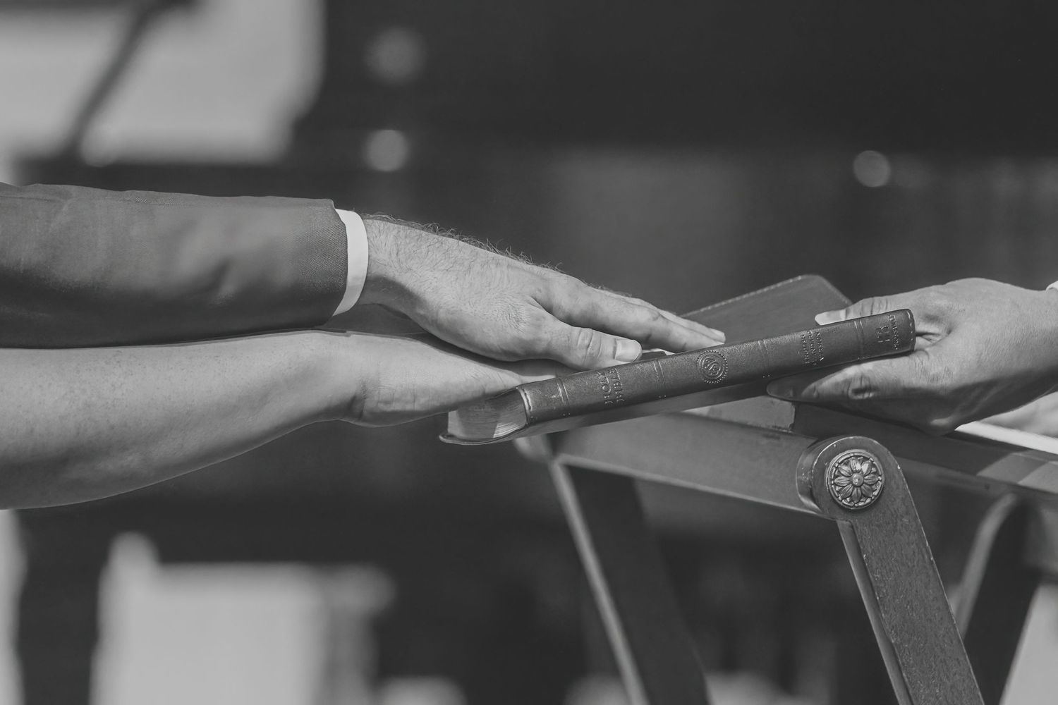 Close-up black and white photo of two people shaking hands over a wooden table at a formal event.