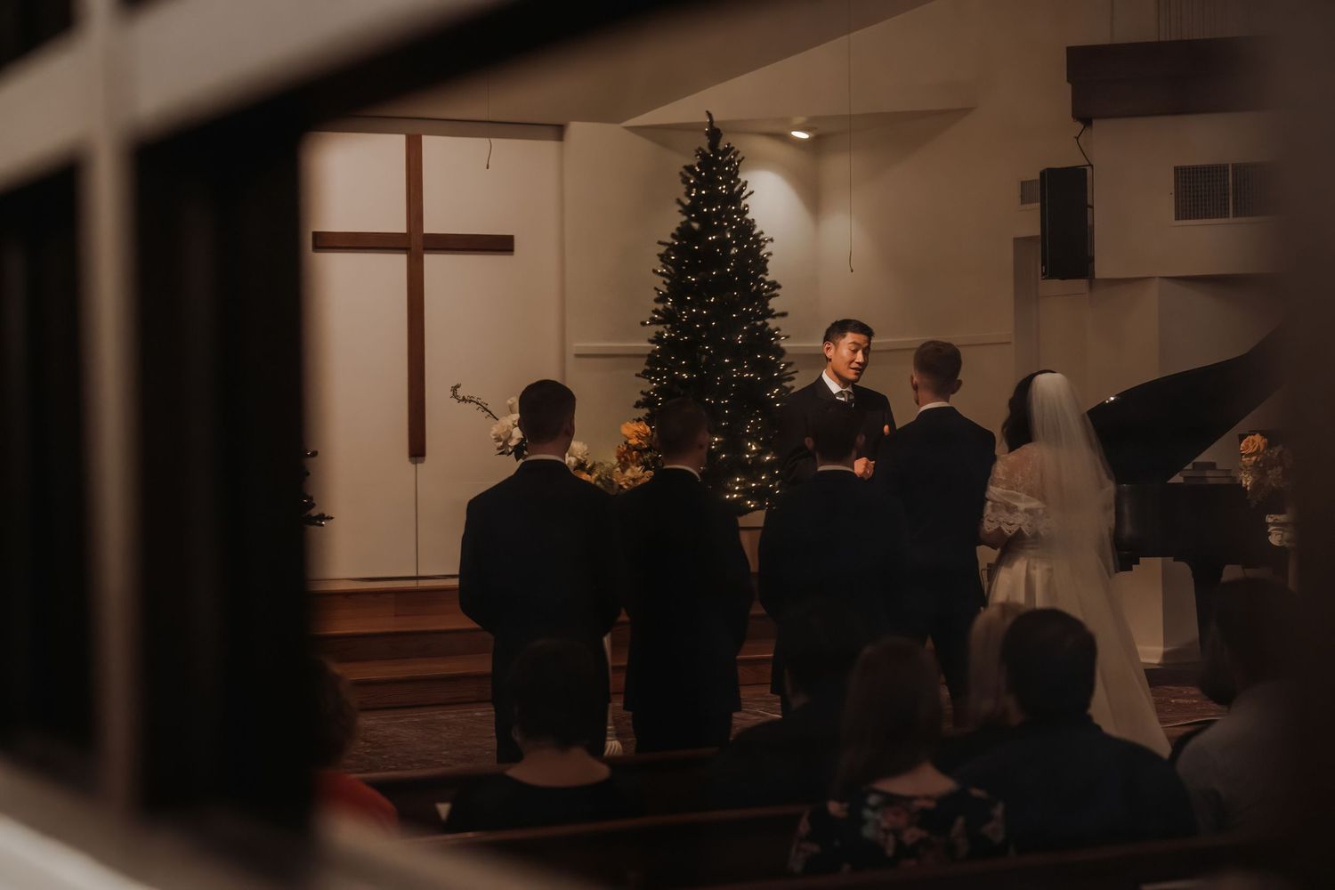 Wedding ceremony in a church with a Christmas tree, cross, and officiant addressing the wedding party.