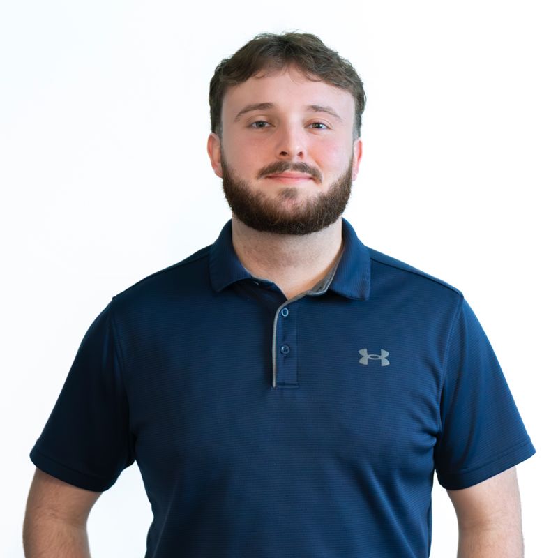 Professional headshot of person in navy Under Armour polo against white background.