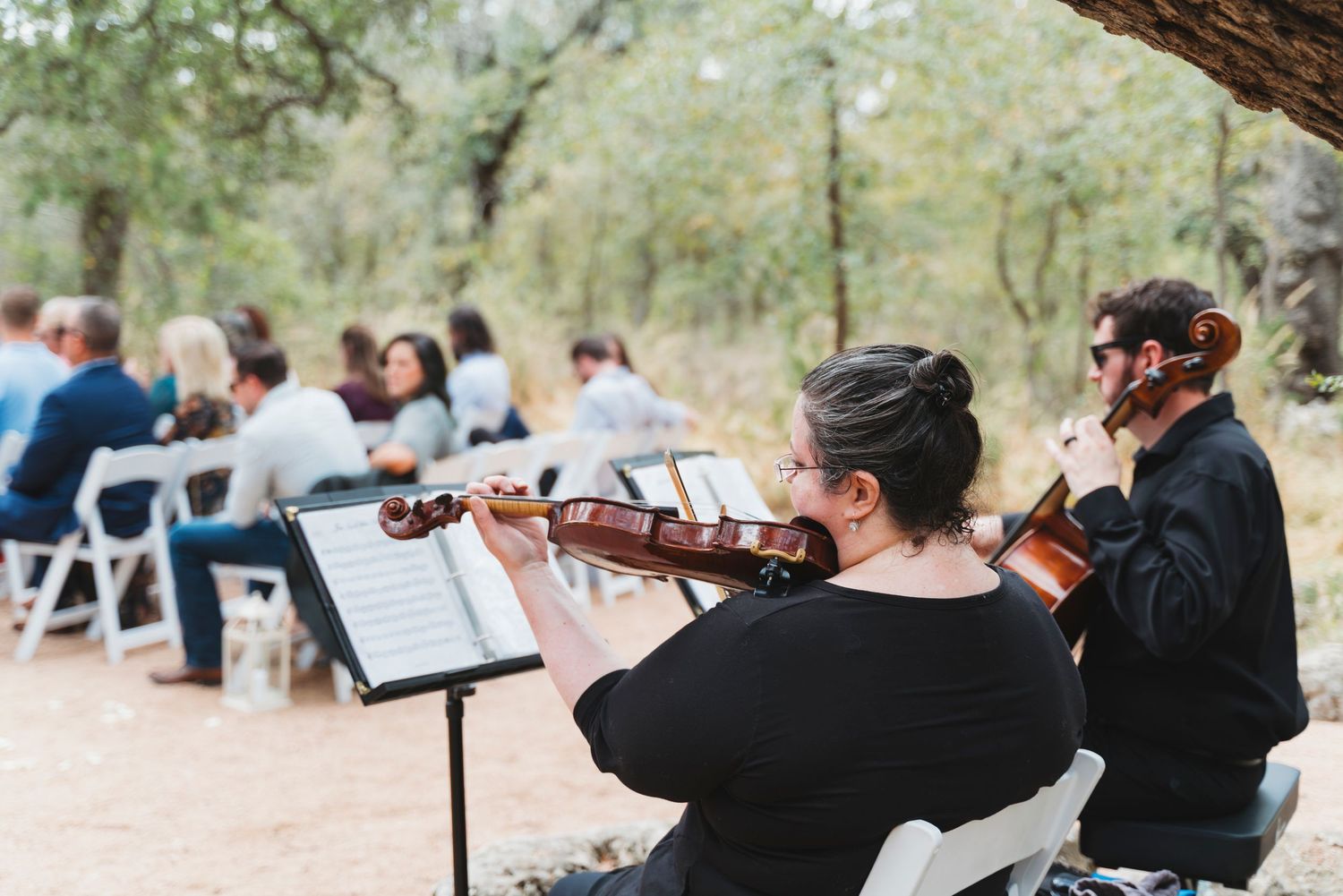 String quartet performing outdoors at a wedding ceremony with guests seated among trees.