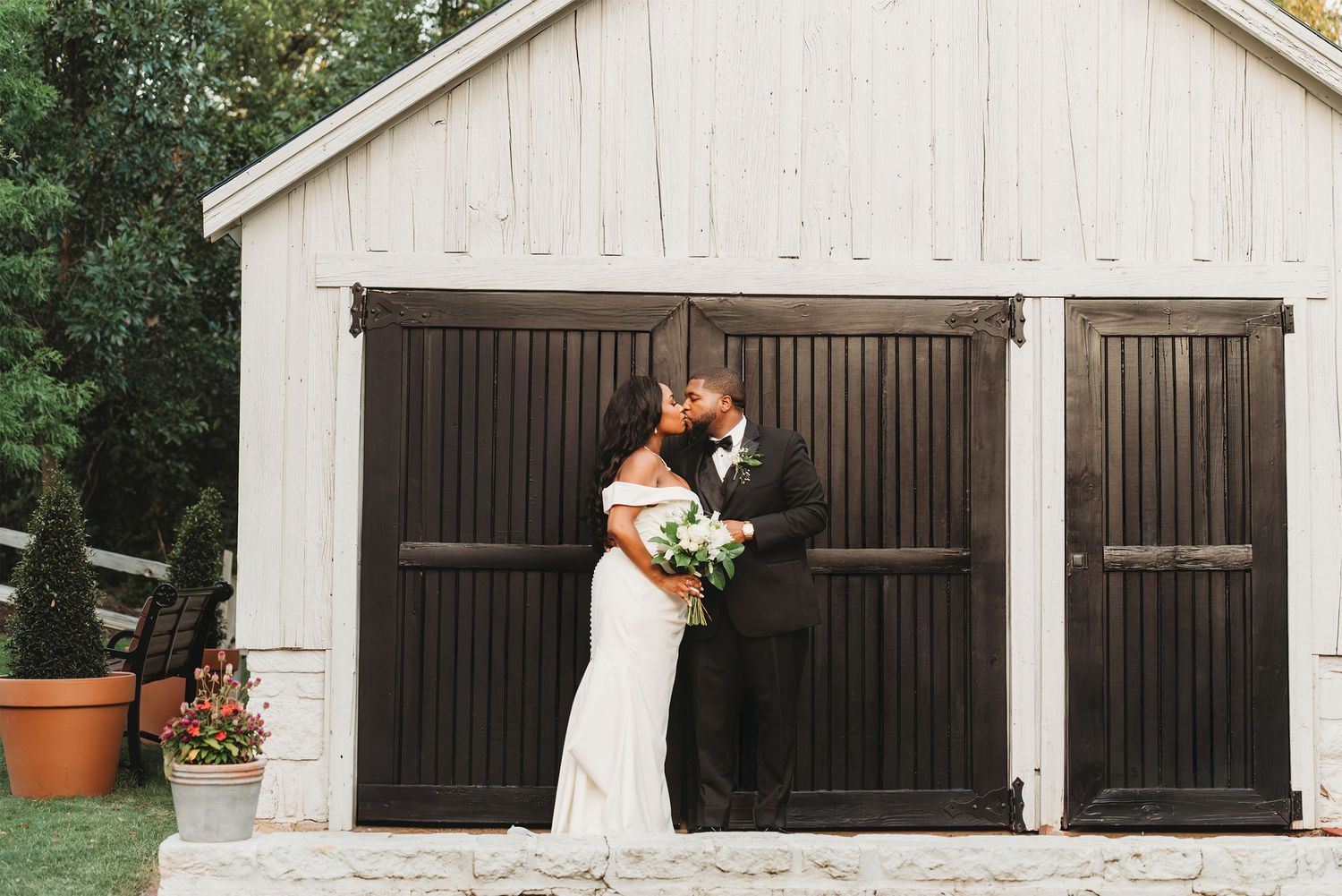 Bride and groom kissing in front of white barn doors wedding photography Waco TX Sudden Joy Visuals