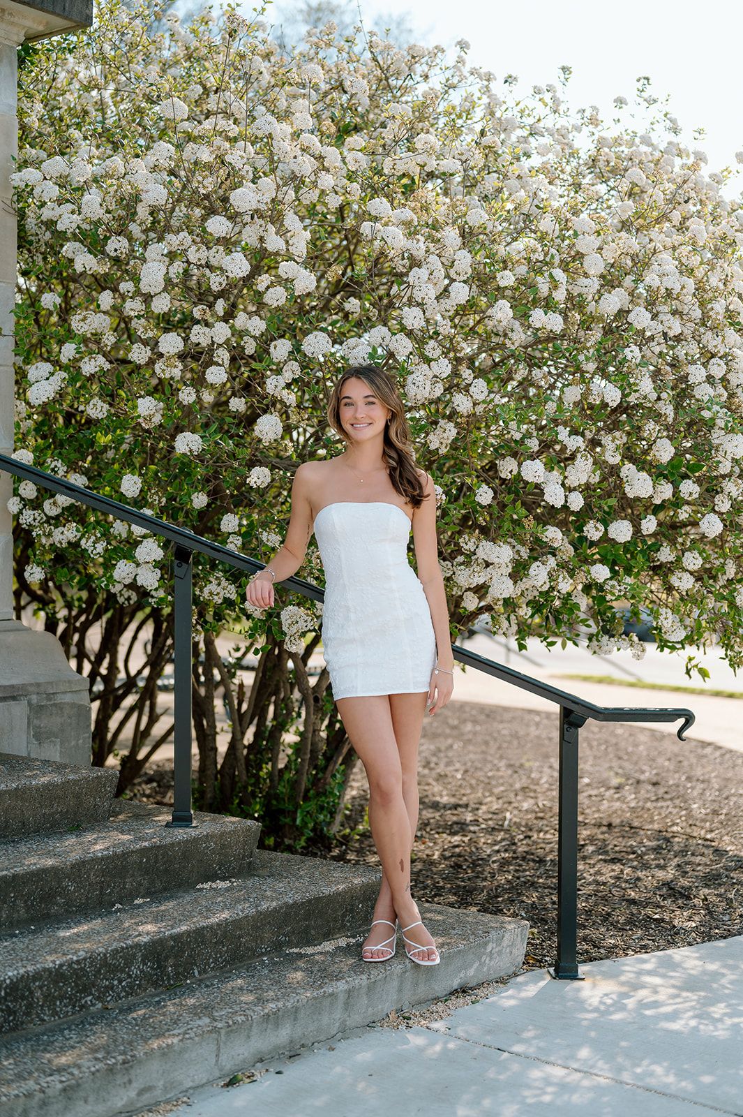 Outdoor portrait session featuring white dress and flowering rose bushes.